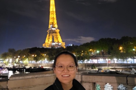 Kaijia is standing smiling in front of the illuminated Eiffel Tower at night.
