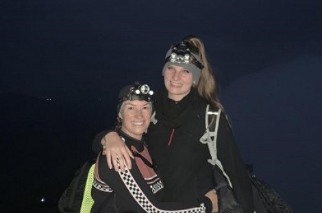 Madeleine and a friend stand grinning with their arms around each other at the summit of Snowden. It is still dark, so they are wearing head torches.
