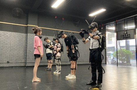 Yujun and other members of the team are wearing virtual reality headsets and equipment for a team-building exercise. The person closest to the camera is reaching out his arms to something in the exercise.